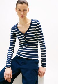 T-shirt à manches longues rayé bleu marine et blanc avec un col en V et trois boutons au niveau du col. Le tissu semble doux et extensible.