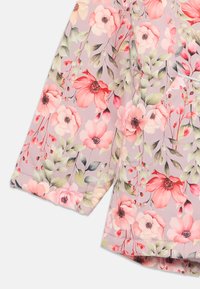 Blouse florale présentant un fond violet clair avec des fleurs roses et rouges. Manches courtes, texture douce et finitions en ourlet cousu.