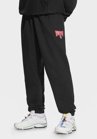 Czarne dresy z czerwonym logo "Presto" na lewym udzie, z elastycznym paskiem w talii i mankietami, połączone z białymi butami sportowymi.