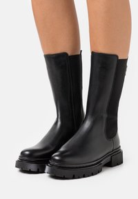 Mustat nahkaiset nilkkasaappaat, joissa on sileä pinta, elastiset sivupaneelit ja kestävät kumipohjat, joissa on teksturoitu reuna.