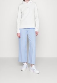 Sudadera blanca con capucha y logo de Calvin Klein, combinada con pantalones de pierna ancha azul claro y zapatillas blancas con detalles en azul claro.