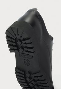 Μαύρο δερμάτινο παπούτσι με υφασμάτινη σόλα από καουτσούκ, που διαθέτει βαθιές αυλακώσεις για πρόσφυση και αντίθετη ραφή κατά μήκος των άκρων.