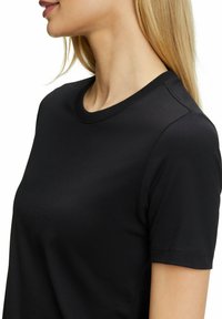 Czarna koszulka z krótkim rękawem o gładkiej fakturze i klasycznym dekolcie. Posiada minimalne szwy na szwach ramion.