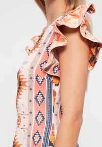 Φορεμα με μοτίβο που διαθέτει έναν συνδυασμό πορτοκαλί, μπλε και ροζ αποχρώσεων. Ραμμένα μανίκια με υφή και γεωμετρικά σχέδια κατά μήκος του σώματος.