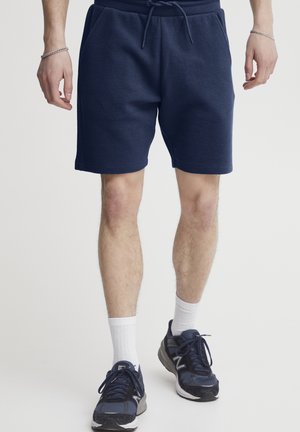 Mørkeblå bomullsblendshorts med et teksturert mønster, elastisk livlinje, snøring og sidelommer. Bært med mørke joggesko og hvite sokker.