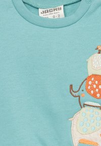 Hellblaues Baumwollbabyshirt mit Rundhalsausschnitt, ausgestattet mit einem bestickten Tierdesign in Orange, Creme und Petrol sowie mit Punkten.