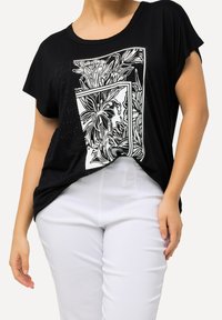 Černé tričko s krátkým rukávem, zdobené bílou květinovou grafikou a akcenty z rhinestone, spárované s přiléhavými bílými kalhotami. Hladká textura, uvolněný střih.
