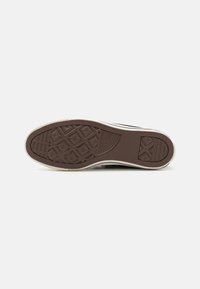 Suela de zapatilla de goma marrón con un diseño de tracción, que presenta líneas diagonales y formas hexagonales. Acento de media suela blanca y bordes texturizados.