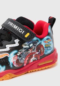 Crne tenisice s crvenim naglascima, s čičak trakama. Grafika monster trucka i plamena s bočne strane, teksturirani mrežasti jezik, gumeni potplat.