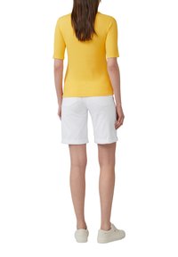 Haut jaune à rayures à manches courtes associé à un short en denim blanc avec ourlet roulé. Le modèle porte des baskets de couleur claire, montrant un look décontracté.