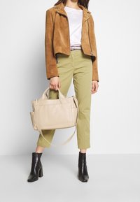 Bolso de cuero beige con dos asas superiores y una correa desmontable, combinado con una chaqueta corta de ante marrón, pantalones verde oliva y botines negros.