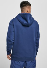 Sötétkék kapucnis pulóver puha pamut keverékből, nagy kapucnival, bordázott mandzsettákkal és aljjal, sima felülettel és letisztult dizájnnal.