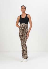 Crna rebrasta majica bez rukava s tri gumba; hlače s leopard printom visokog struka u bež i crnoj boji; bijele tenisice; glatka tekstura.