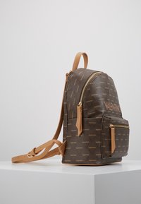 Brun mönstrad ryggsäck med beige läderdetaljer. Har ett huvudfack med dragkedja och en framre dragkedjeficka. Justerbara axelremmar.