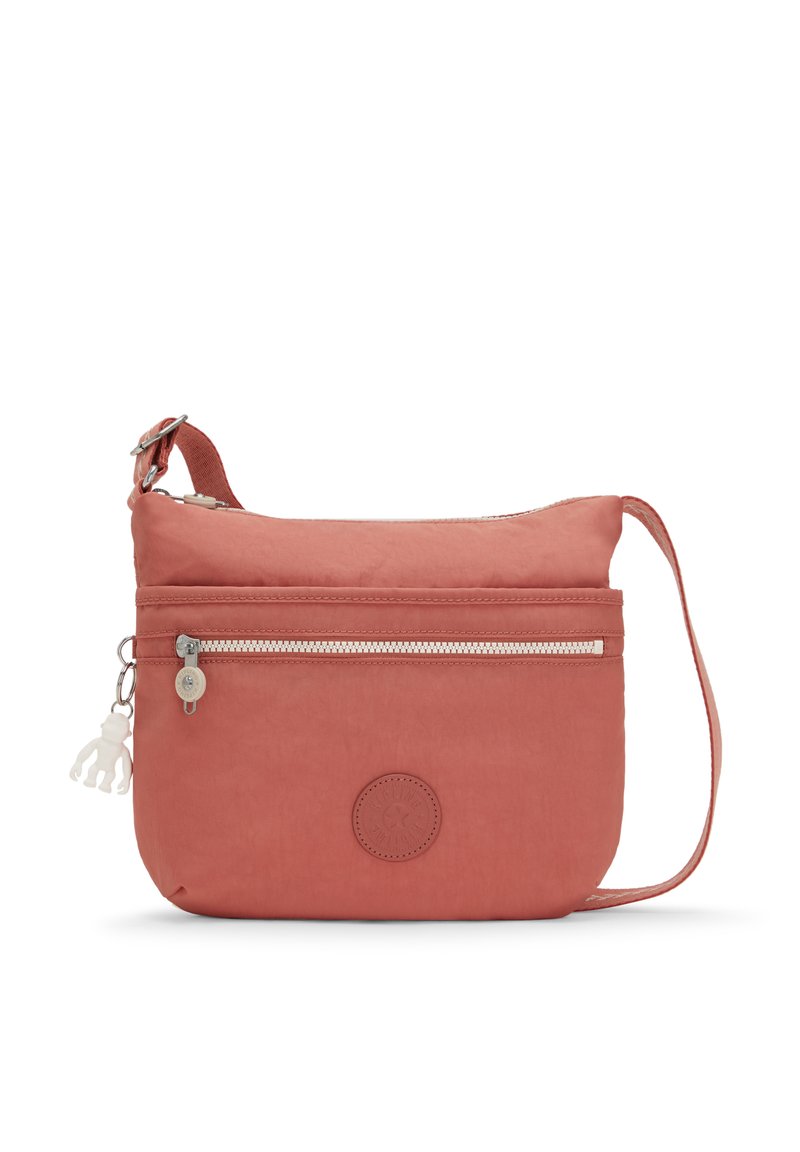 Malá korálová crossbody taška s přední kapsou na zip, nastavitelným popruhem a bílým přívěskem ve tvaru opice.