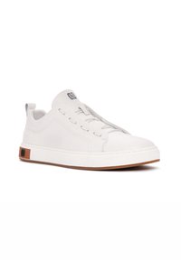 Zapatilla blanca con parte superior sintética suave, suela de goma y sutiles acentos en gris. Cuenta con un diseño de cordones y el logo en la lengüeta.
