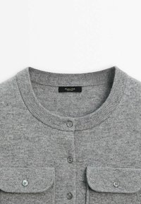 Cardigan en maille gris clair avec col rond, boutons sur le devant et deux poches poitrine à boutons, posé à plat sur fond blanc.