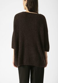 Pull oversized en tricot marron avec un col rond côtelé et des manches trois-quarts, présentant un tissu doux et texturé.
