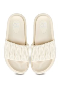 Sandales à glissière moulées beiges avec une sangle rembourrée et texturée mettant en avant des coutures en zigzag. Semelles lisses et arrondies pour le confort et le soutien.