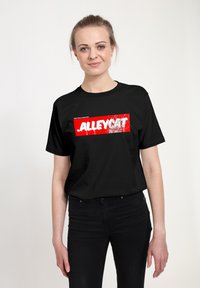 Černé bavlněné tričko s výraznou červenou grafikou s nápisem "ALLEYCAT" bílou barvou, umístěným na pozadí se stříkajícími barvami. Krátké rukávy, kulatý výstřih.