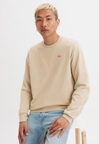 Beige sweatshirt met een ronde hals, voorzien van een klein rood Levi's logo op de linkerkant van de borst. Draagt men met lichtblauwe denim jeans.