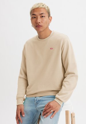 Beige sweatshirt with a crew neckline, featuring a small red Levi's logo on the left chest. Worn with light blue denim jeans.
