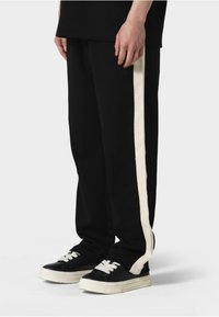 Sorte sweatpants med en elfenbensfarvet sidestreg, lavet af blødt stof med en afslappet pasform. Kombineret med sorte sneakers og hvide snørebånd.