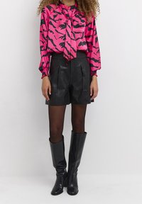 Różowa i czarna jedwabna bluzka w nadruk z wiązaniem przy szyi, połączona z czarnymi skórzanymi szortami o wysokim stanie i błyszczącymi czarnymi kozakami do kolan.