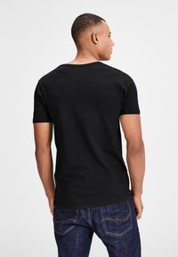 Schwarzes Baumwoll-T-Shirt mit rundem Halsausschnitt und kurzen Ärmeln, von hinten betrachtet, kombiniert mit blauen Denim-Jeans mit dezentem Nähen.