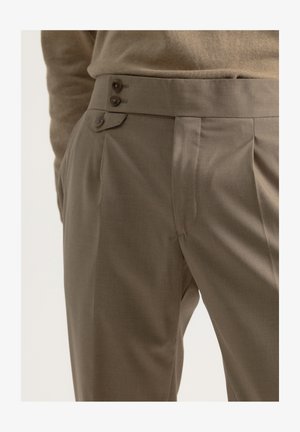 Pantalones a medida en una tela marrón apagado, con frente plano, pliegues marcados, dos botones en la cintura y una textura suave.