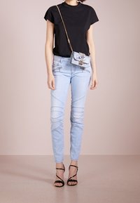 Camiseta negra de manga corta, jeans skinny azul claro con detalles bordados y tacones negros con tiras. Bolso de hombro pequeño con adornos.