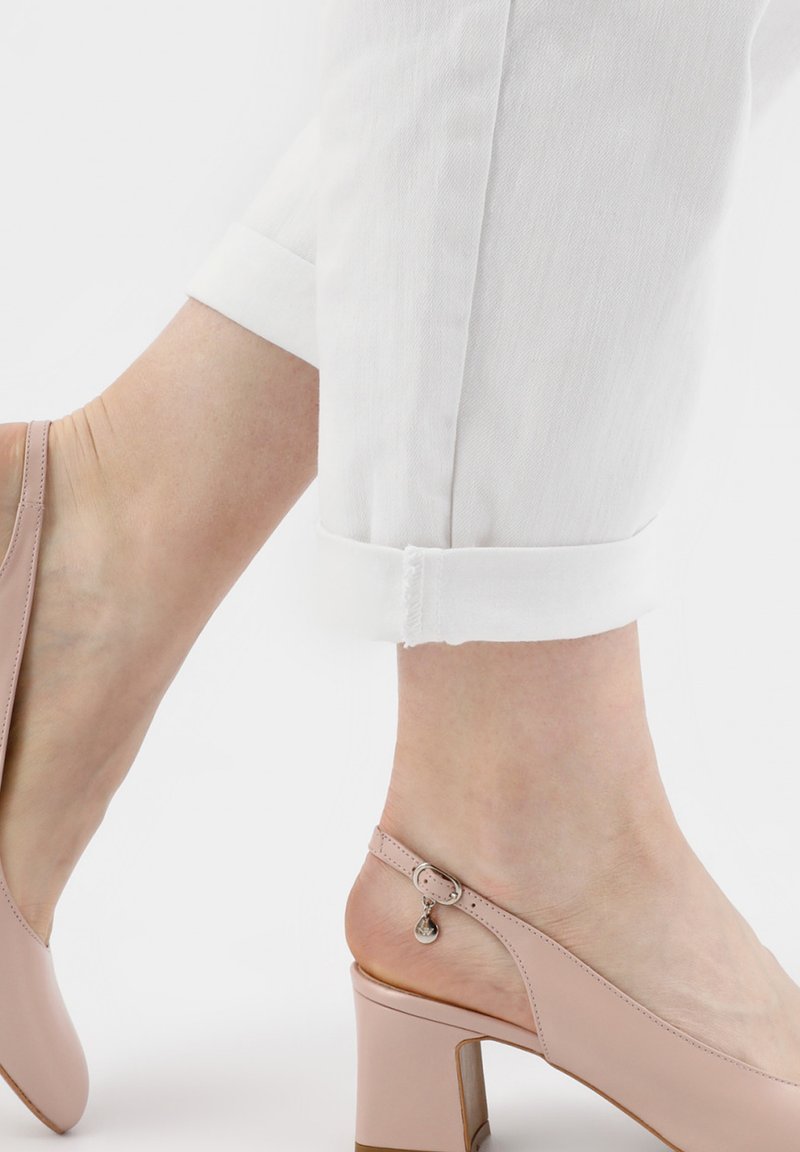 Escarpins slingback rose blush avec bout arrondi, talon bloc et bride de cheville ajustable ornée d'un petit détail métallique. Portés avec un pantalon blanc retroussé.