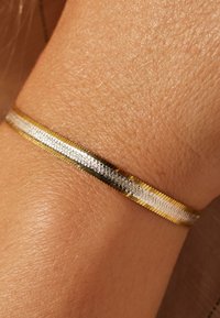Gold and silver bangle bracelet, featuring a flat design with alternating metal colors and a textured surface, worn on a wrist.