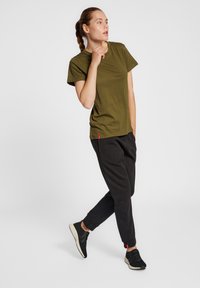 Oliven grøn bomulds t-shirt med korte ærmer, parret med sorte sweatpants. Bukserne har sidelommer og en rød labeldetalje. Sorte sportssko.