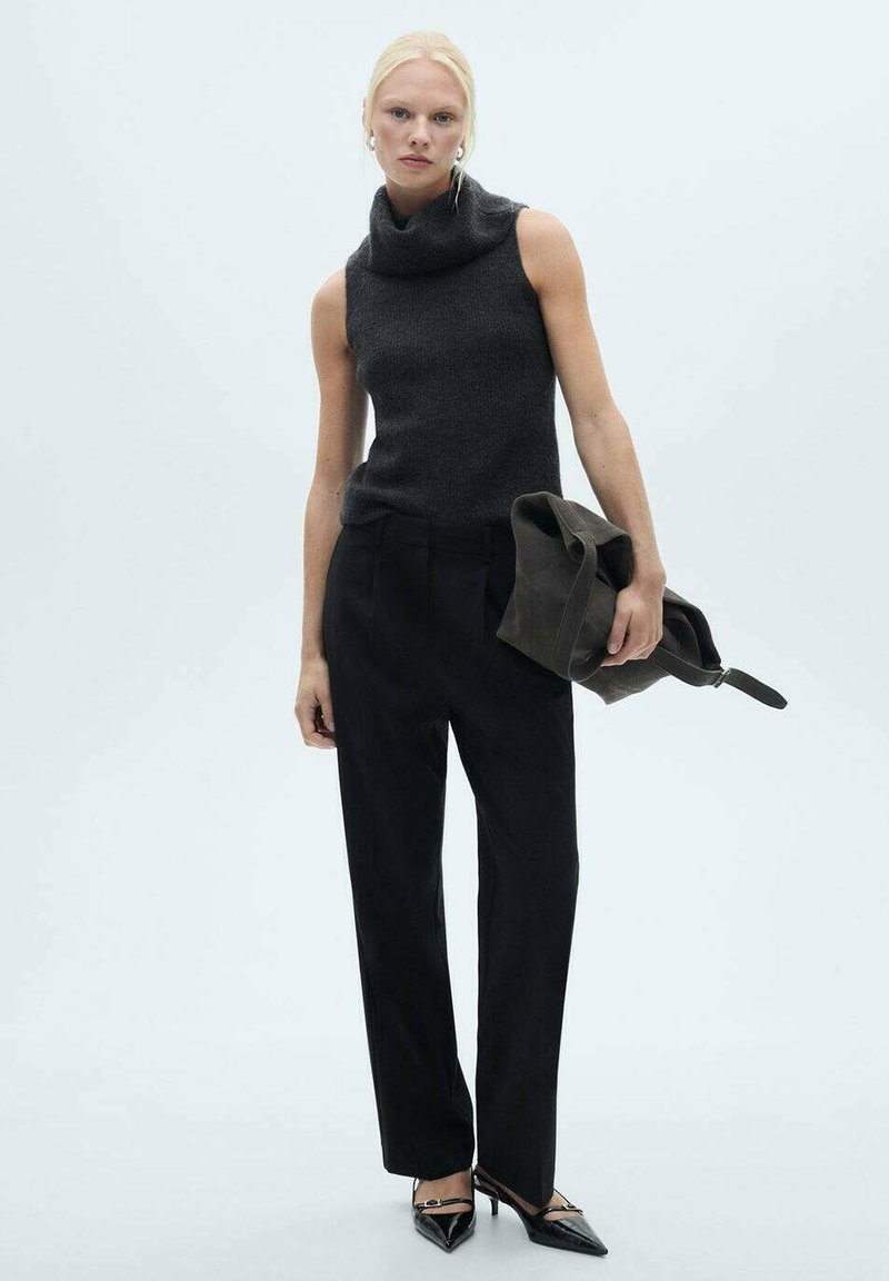Szary bezrękawnik z golfem o fakturowanym wykończeniu w zestawieniu z czarnymi dopasowanymi spodniami i czarnymi szpilkami, trzymając ciemną torbę.