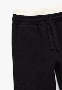 Zwarte, geweven sweatpants met een crèmekleurige elastische tailleband, voorzien van zijzakken en een trekkoord voor aanpassing.