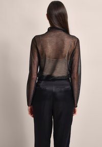 Durchsichtiges schwarzes Langarmoberteil mit kragen, strukturiertem Stoff und cropped Design, kombiniert mit hoch taillierten schwarzen Hosen.