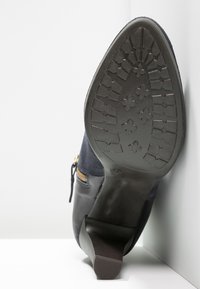 Stivale nero e blu con suola in gomma texturizzata, motivo del battistrada geometrico e un accento con cerniera. Pannello laterale in suede blu.