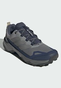 Graue und marineblaue Sportschuhe aus Netzmaterial, mit strukturierten Akzenten, Gummisohle und reflektierenden Details. Verfügt über eine Schnürung und ein Logo.