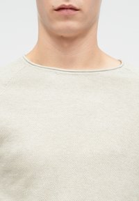 Maglione a maglia grigio chiaro con scollatura rotonda, caratterizzato da un tessuto testurizzato e maniche raglan. Finitura liscia e dettagli di design minimali.