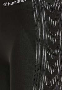 Leggings atléticos negros con un patrón texturizado que presenta rayas verticales y diseños en forma de flecha en blanco contrastante.