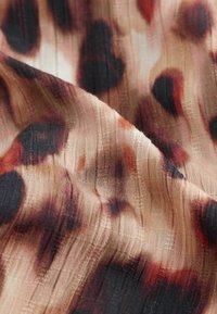Tissu doux avec un motif texturé en forme de grille et de grandes taches noires et brun-rougeâtres irrégulières sur un fond beige.