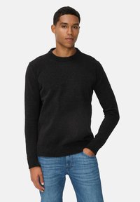 Schwarzer, gestrickter Pullover mit Rundhalsausschnitt, gerippten Bündchen und Saum. Über hellblauen Jeans getragen. Glatte Textur mit subtilen Mustern.