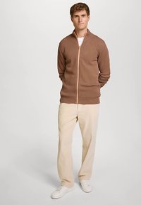 Maglione marrone con cerniera, con motivo testurizzato e cerniera pesca a contrasto, abbinato a pantaloni crema a coste e sneaker bianche.