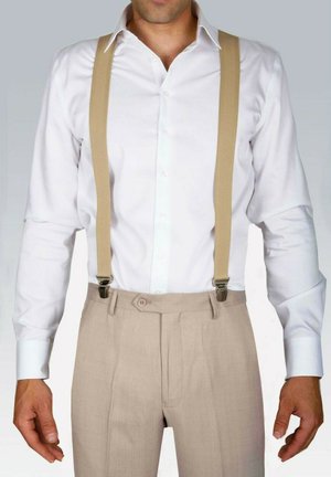 Chemise blanche à col, bretelles beiges et pantalon plissé beige clair avec fermeture à boutons. Tissu lisse, coupe classique, quincaillerie minimale.