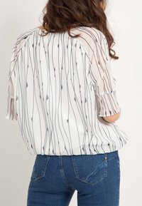 Blouse légère et transparente avec des rayures verticales bleu marine sur fond blanc. Caractérisée par des manches courtes plissées et une coupe décontractée.