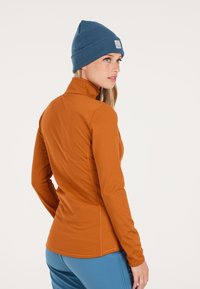 Oranje langemouwen top met een hoge kraag, slim fit en platte naden. Gecombineerd met een blauwe geribbelde beanie met een logo patch.
