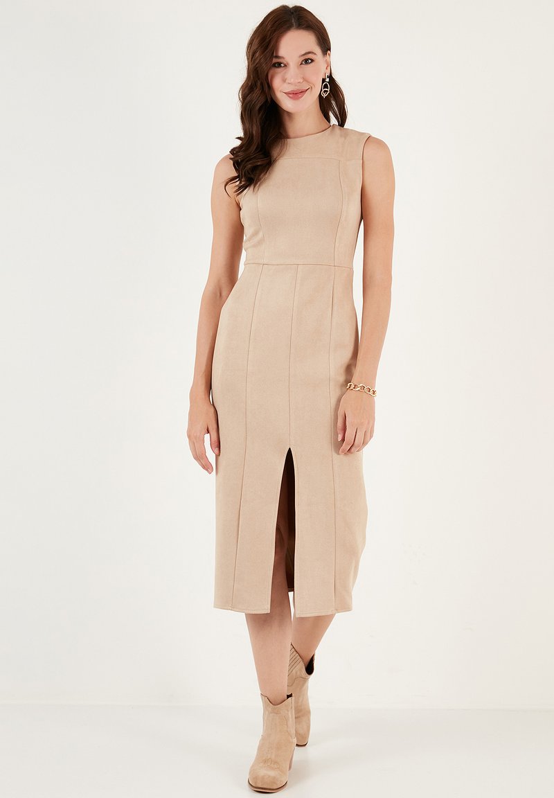 Robe midi sans manches en suède beige avec une silhouette ajustée, fente avant et détails de panneaux ; associée à des bottines beige clair.