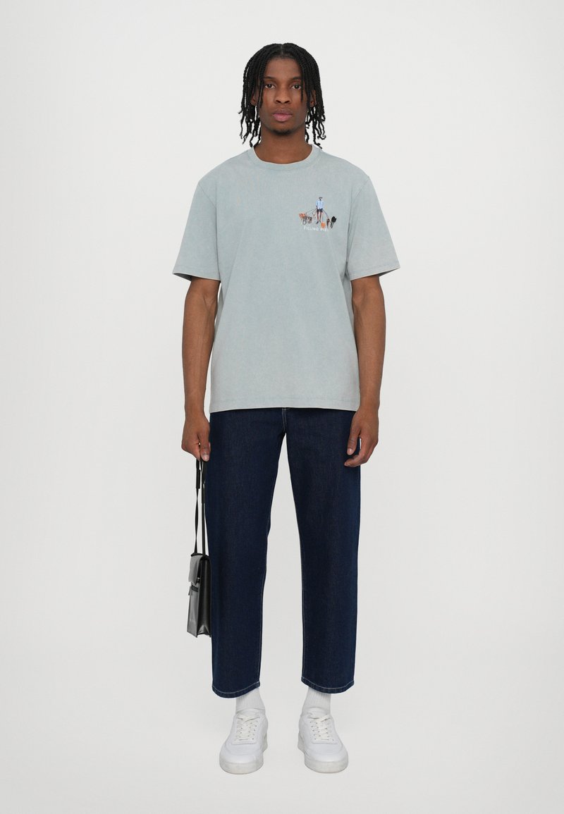 T-shirt di cotone azzurro chiaro con una piccola stampa grafica sul petto, abbinata a jeans dritti blu scuro e sneaker bianche.