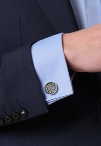 Marineblauer Anzug mit einem hellblauen Hemdärmel, der einen runden silbernen Manschettenknopf zeigt, der ein schwarzes geometrisches Muster und einen strukturierten Stoff aufweist.